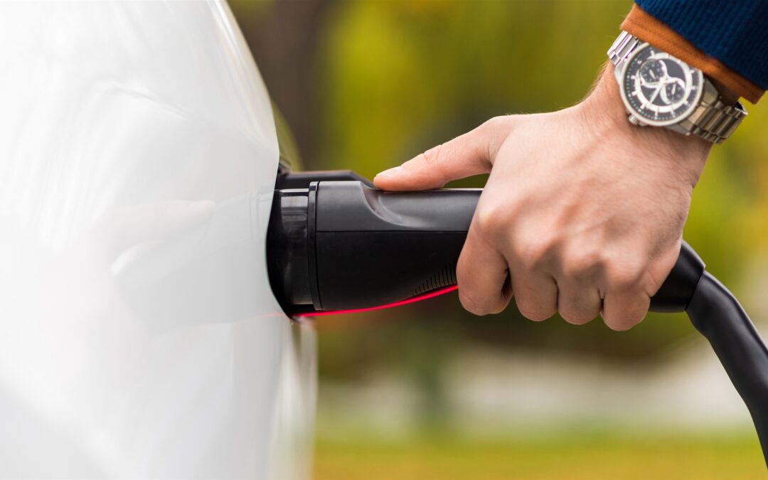 Hand steekt een laadstekker in een elektrische auto